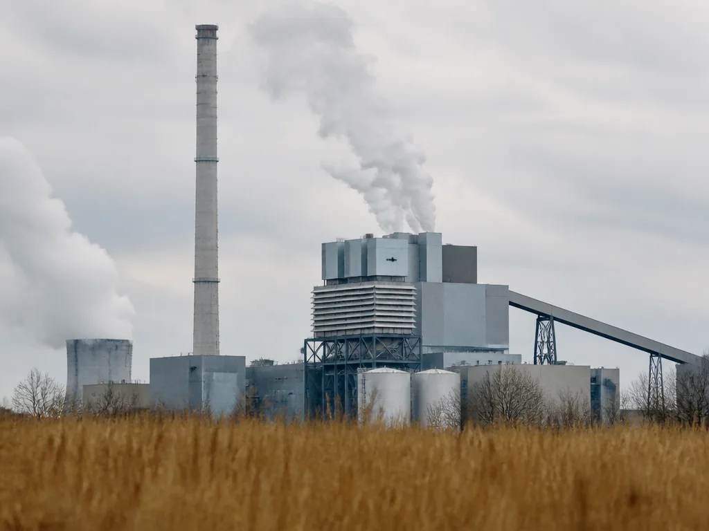 Industriellt kraftvärmeverk med skorsten och ånga mot mulen himmel